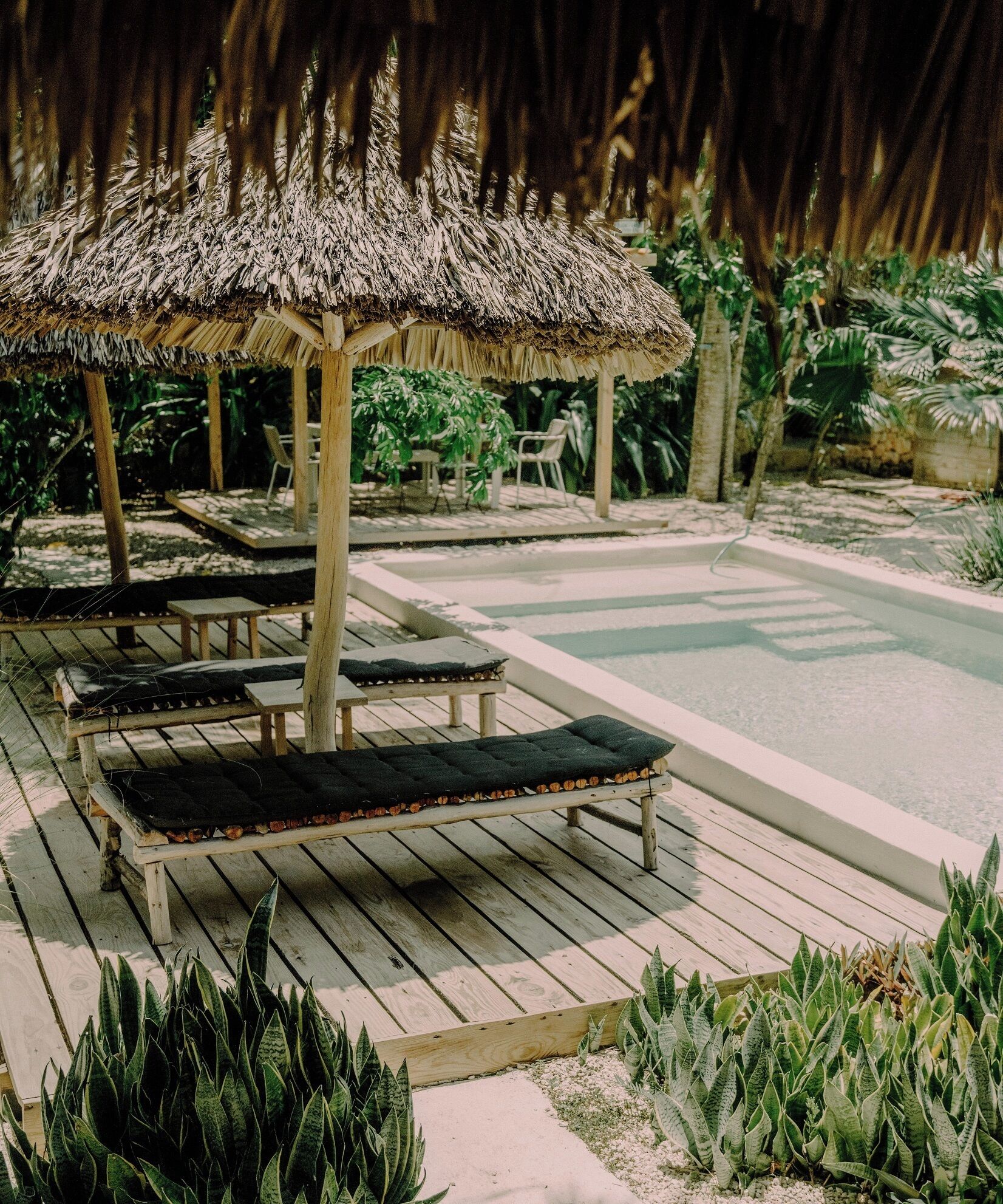 A wooden deck with lounge chairs and a thatched-roof gazebo.