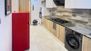 Uma cozinha moderna com frigorífico vermelho, forno embutido, máquina de lavar roupa e painel de parede em pedra.