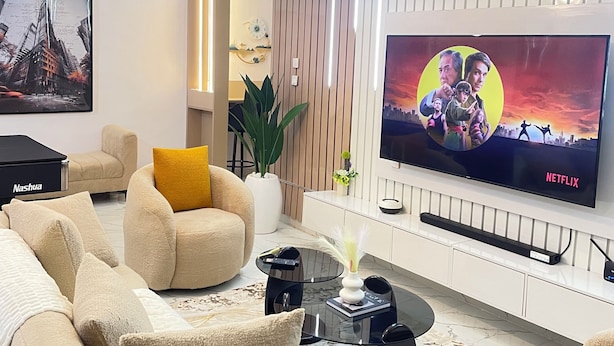 Uma sala de estar moderna com uma televisão de tela plana grande fixada na parede, um sofá confortável, uma mesa de centro e uma planta decorativa.