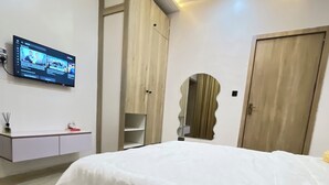 Quarto com cama, televisão na parede, guarda-roupa e espelho.