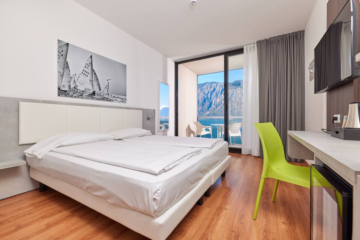 A hotel room with a bed, a desk, a chair, a TV, and a painting of sailboats.