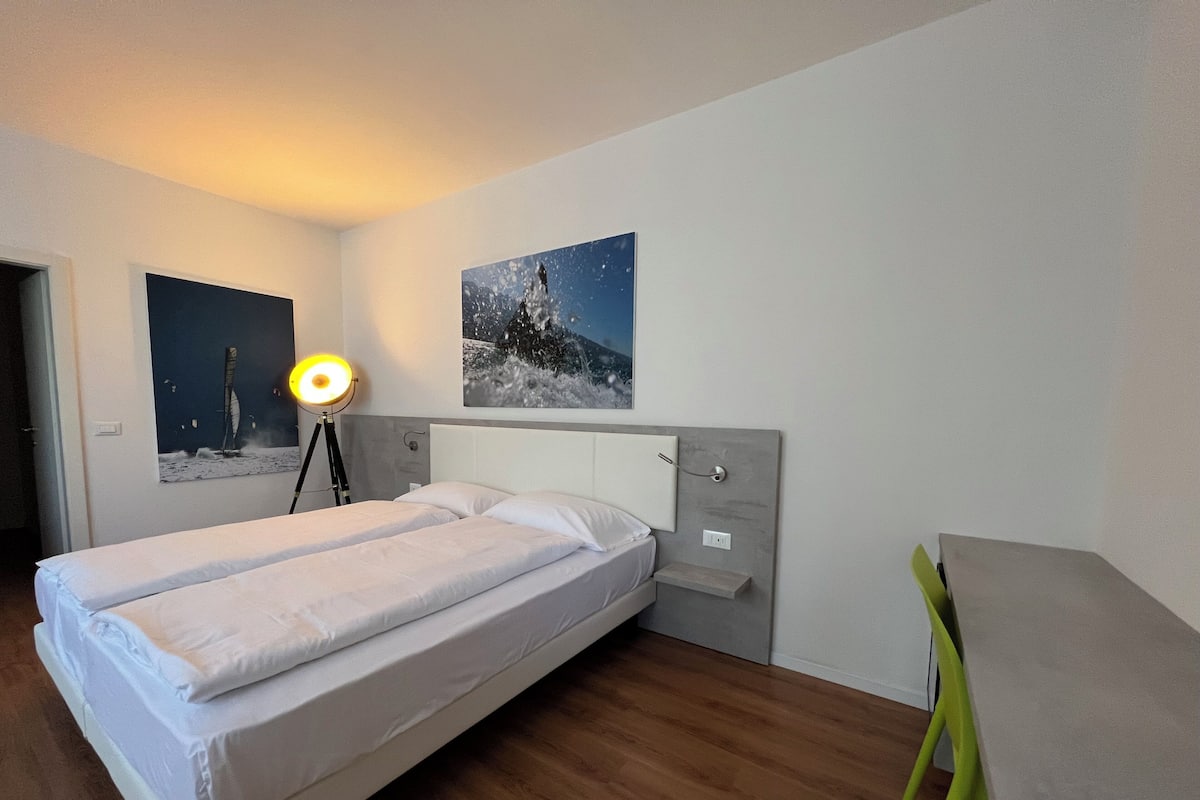 A hotel room with a bed, a desk, and two wall-mounted pictures.