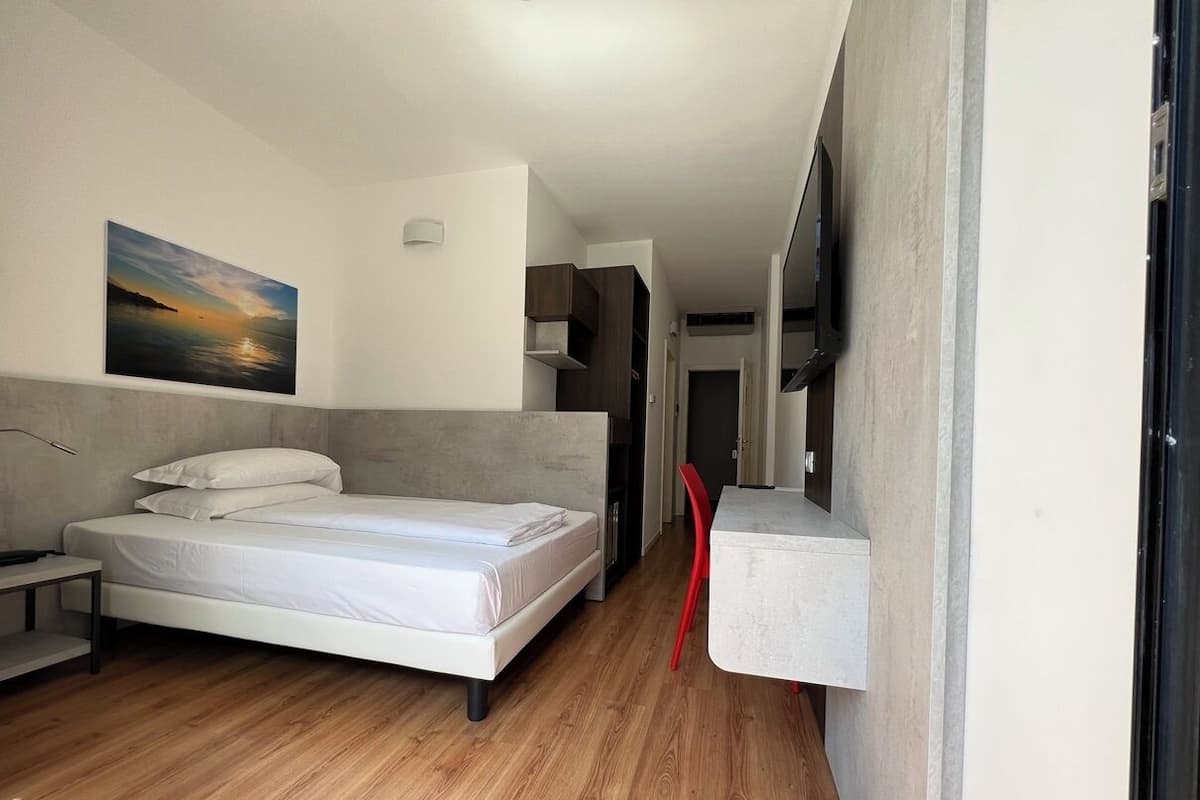 A modern bedroom with a bed, a small table, and a TV mounted on the wall.