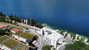 An aerial view of a coastal area with modern buildings, a road, and a clear blue sea. - WIND HOTEL (Malcesine)