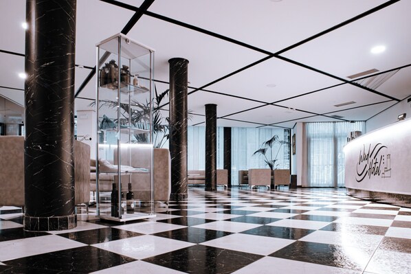 Un hall d’hôtel avec un sol à carreaux, des colonnes de marbre et un comptoir d’accueil.