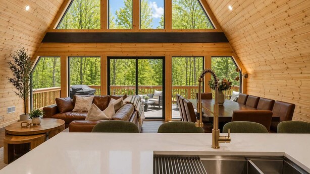 A spacious loft-style room with a large dining table, leather seating, and a kitchen area. - Iconic A-Frame | Hot Tub | Fire Pit | Walk to Lake | Near Ski Resorts (Blakeslee)