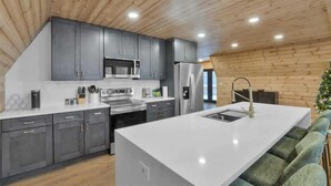 A modern kitchen with grey cabinets, stainless steel appliances, and a white island. - Iconic A-Frame | Hot Tub | Fire Pit | Walk to Lake | Near Ski Resorts (Blakeslee)