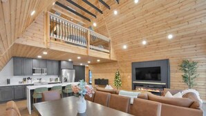 A spacious living area with a high ceiling, a fireplace, and a balcony. - Iconic A-Frame | Hot Tub | Fire Pit | Walk to Lake | Near Ski Resorts (Blakeslee)