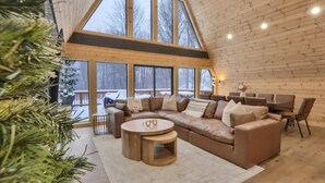 A cozy living room with a large wooden ceiling, a sectional sofa, and a round coffee table. - Iconic A-Frame | Hot Tub | Fire Pit | Walk to Lake | Near Ski Resorts (Blakeslee)