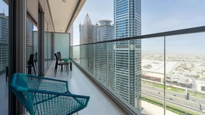 Ein Balkon mit Blick auf hohe Gebäude, einem Tisch mit Stühlen und einem grünen Sessel.