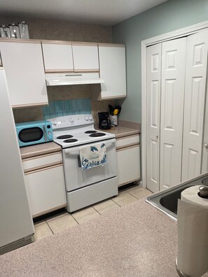 Una cocina con armarios blancos, un microondas azul, una estufa con una toalla y una puerta con picaporte.