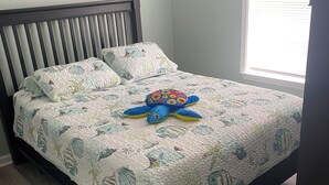 A bed with a floral quilt, a wooden headboard, and a window with blinds. - Welcome to Steve & Tracie’s Gulf Retreat!  (Gautier)