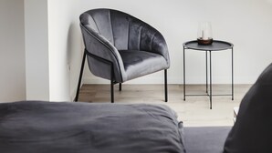 Une chambre moderne avec un plafond en pente, un fauteuil en cuir, une petite table ronde avec un verre et un lit.