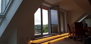 A room with a sloped ceiling, large windows, and a wooden table with chairs. - Holiday Apartment 'Habichthorst' with Spacious Loggia, Shared Garden, and Stunning Views (Naumburg)