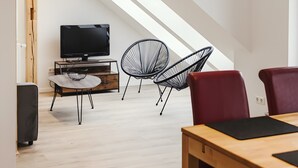 Un intérieur moderne avec un plafond en bois, un téléviseur posé sur un meuble et deux chaises noires.