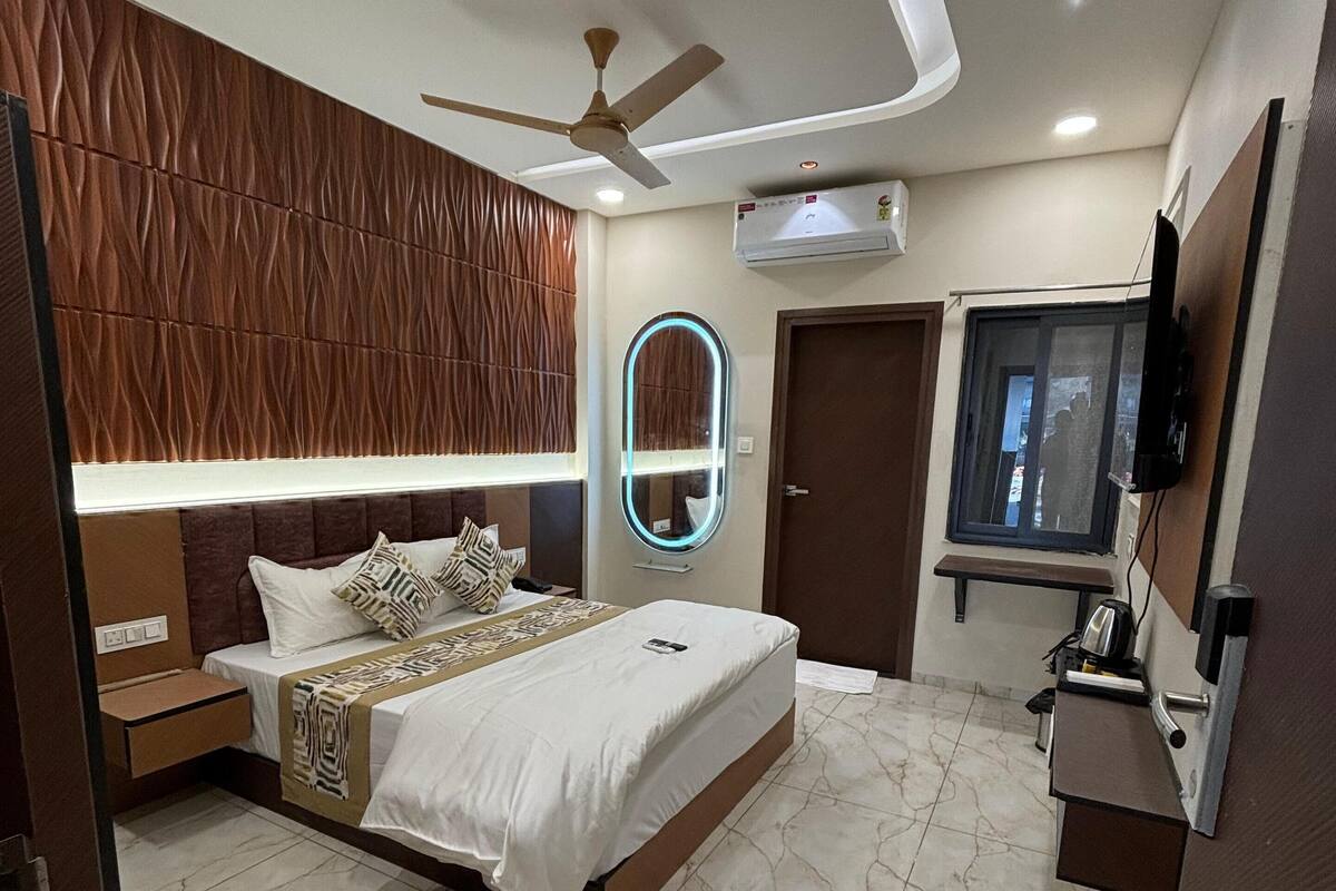 A modern bedroom with a bed, bedside tables, a ceiling fan, an air conditioning unit, a mirror, a TV, and a window.