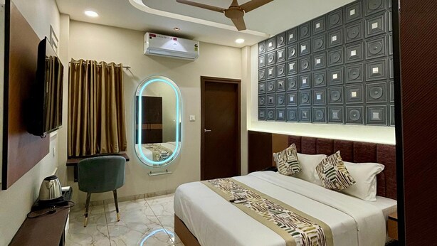 Une chambre d’hôtel moderne dotée d’un grand lit, d’un ventilateur de plafond, d’un appareil de climatisation, d’une télévision, d’un bureau avec une chaise et d’une salle de bain avec un miroir et des rideaux.