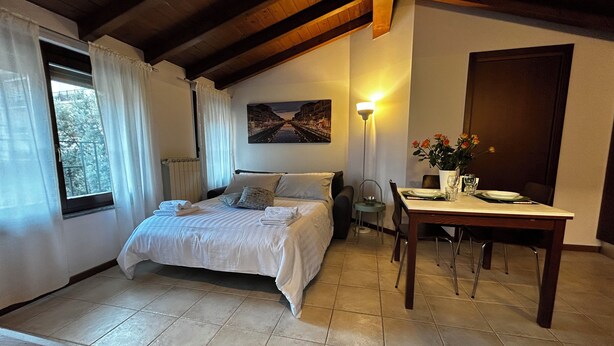 A bedroom with a bed, a dining table with chairs, a lamp, and a painting on the wall.