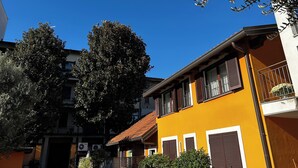 A yellow building with multiple windows and balconies, surrounded by trees and other buildings.