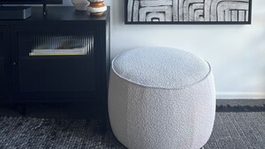 Un salon moderne avec un meuble de rangement noir pour les appareils électroniques, une grande peinture abstraite et un pouf rond de couleur grise.