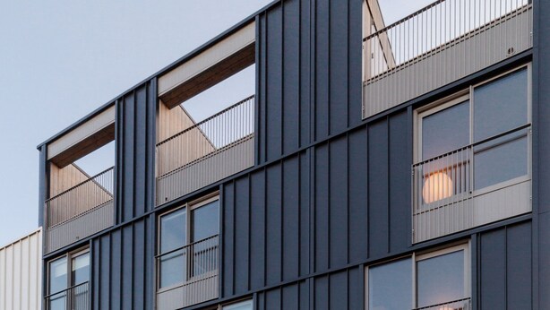 Un bâtiment moderne à la façade sombre, doté de nombreux balcons et de grandes fenêtres.