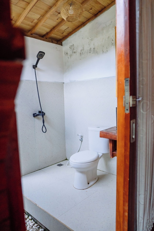 A small, compact bathroom with a white toilet, a shower head mounted on the wall, and a wooden ceiling. - The Caldera Villas Kintamani (Kintamani)