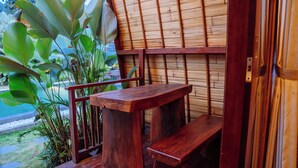 Una terraza de madera con un banco y una mesa, rodeada de plantas verdes grandes.