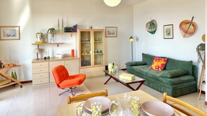 Ein Wohnzimmer mit einem grünen Sofa, einem orangefarbenen Sessel und einem Esstisch, gedeckt mit Tellern und Gläsern.