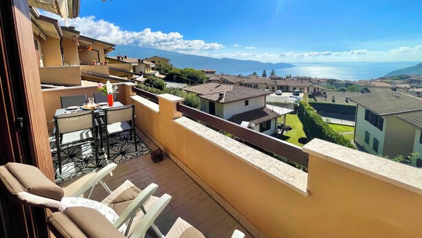 Ein Balkon mit Gartenmöbeln, Blick auf eine Küstenstadt und einem klaren Himmel.