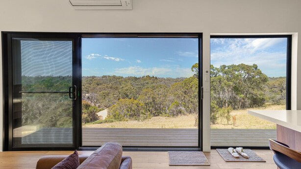 Un salón moderno con un amplio ventanal corredera que ofrece vistas panorámicas al exterior.