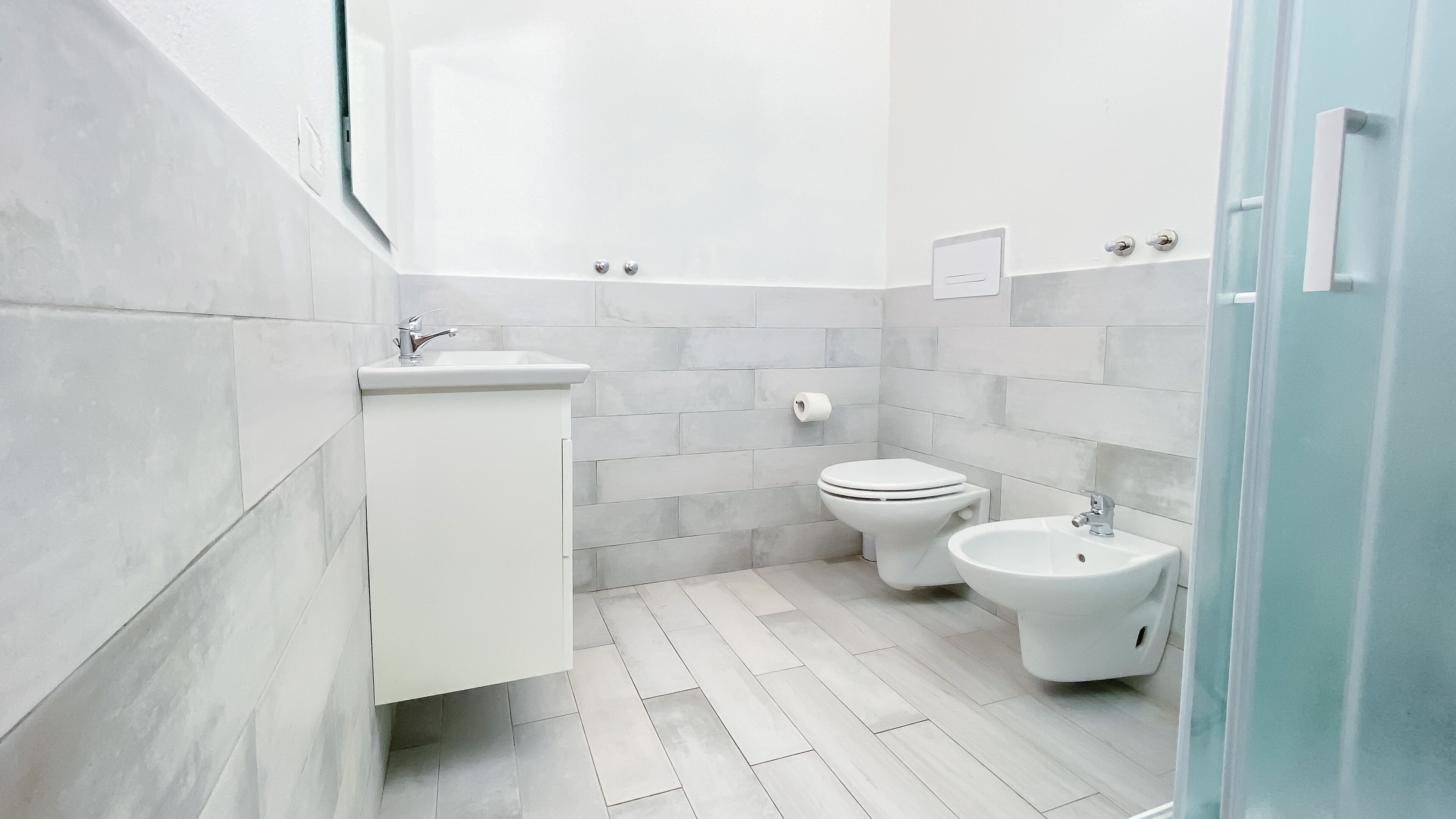 Un baño moderno con un lavamanos blanco, dos inodoros y un bidé.