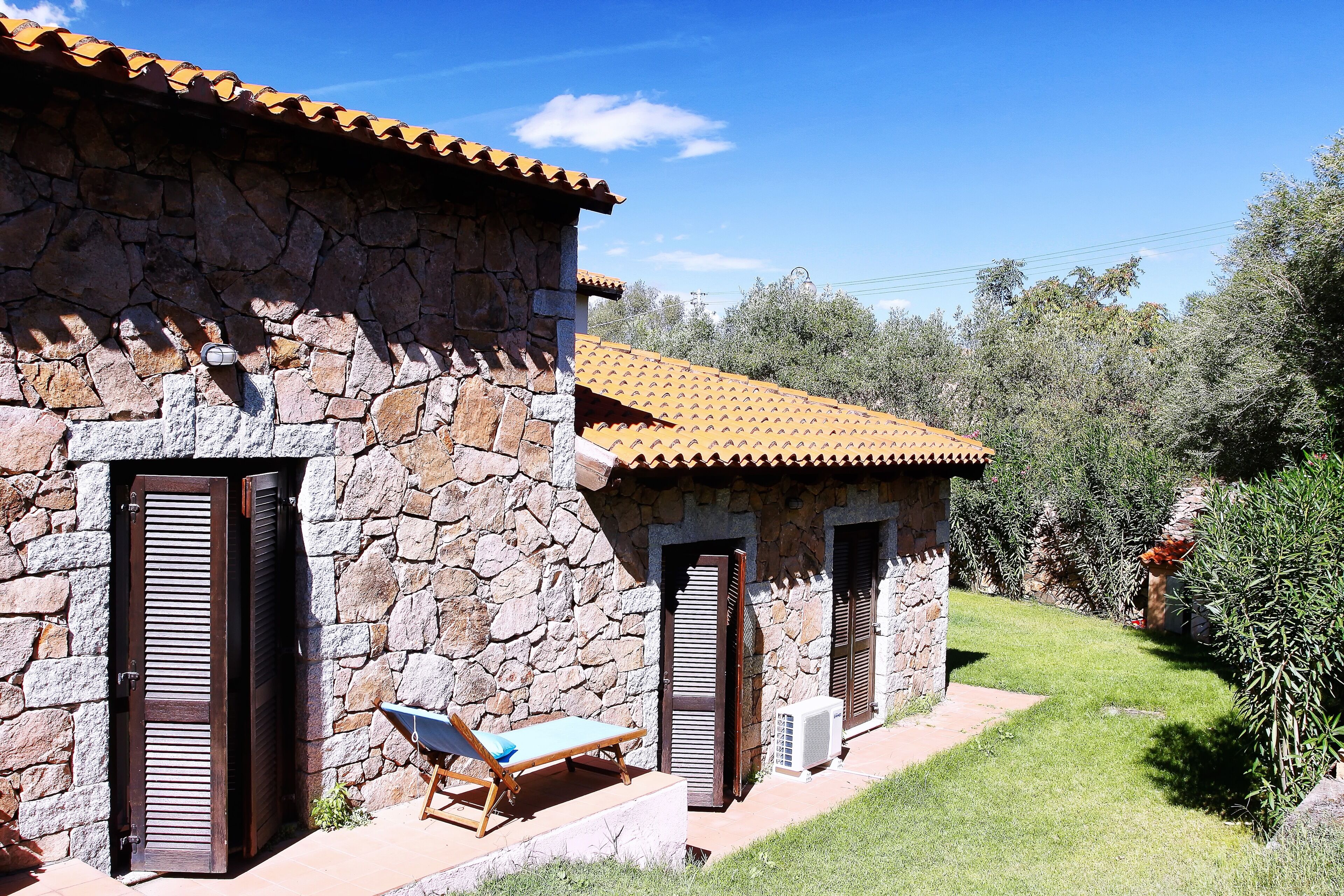 A stone building with a tiled roof, a wooden door, and a small outdoor seating area with a lounge chair.