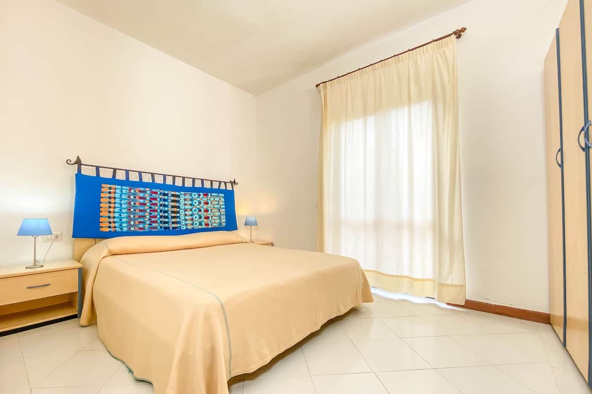 A neatly arranged bedroom with a bed, two bedside tables, a wall-mounted artwork, and a window with curtains.