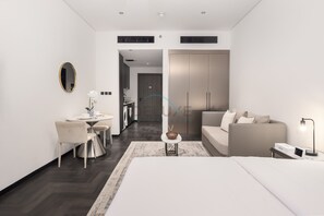 Een moderne hotelkamer met een bed, een slaapbank, een zithoek met een tafel en stoelen, een kleine keuken en een inloopkast.