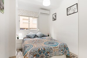 Ein Schlafzimmer mit Bett, Fenster, Klimaanlage und Wandbild.