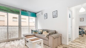 En stue med sofa, sofabord og et stort vindue med udsigt til bygninger.