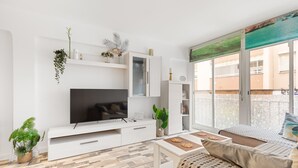 En moderne stue med et fladskærms-TV, hvide skabe, en sofa og en balkon med udsigt.