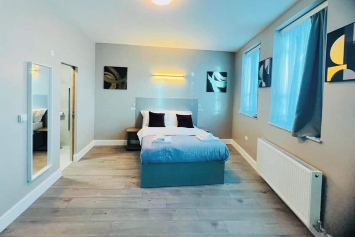 A bedroom with a bed, bedside tables, a wall-mounted light, and artwork.