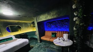A dimly lit room with a bed, a sofa, and a small table with a vase and a bowl. - Paragraph Tottenham (London)