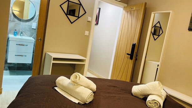 A hotel room with a bed, a bathroom with a mirror, a wooden door, and a shelf. - Paragraph Tottenham (London)