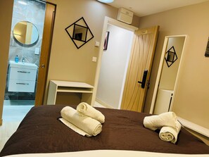 A hotel room with a bed, a bathroom with a mirror, a wooden door, and a shelf. - Paragraph Palmers Green - Tottenham Stadium (London)