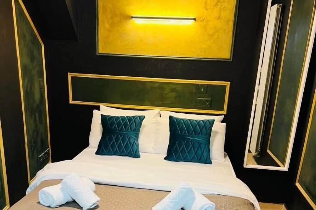 A hotel room with a large bed, two pillows, a bedside table, and a wall-mounted light fixture.