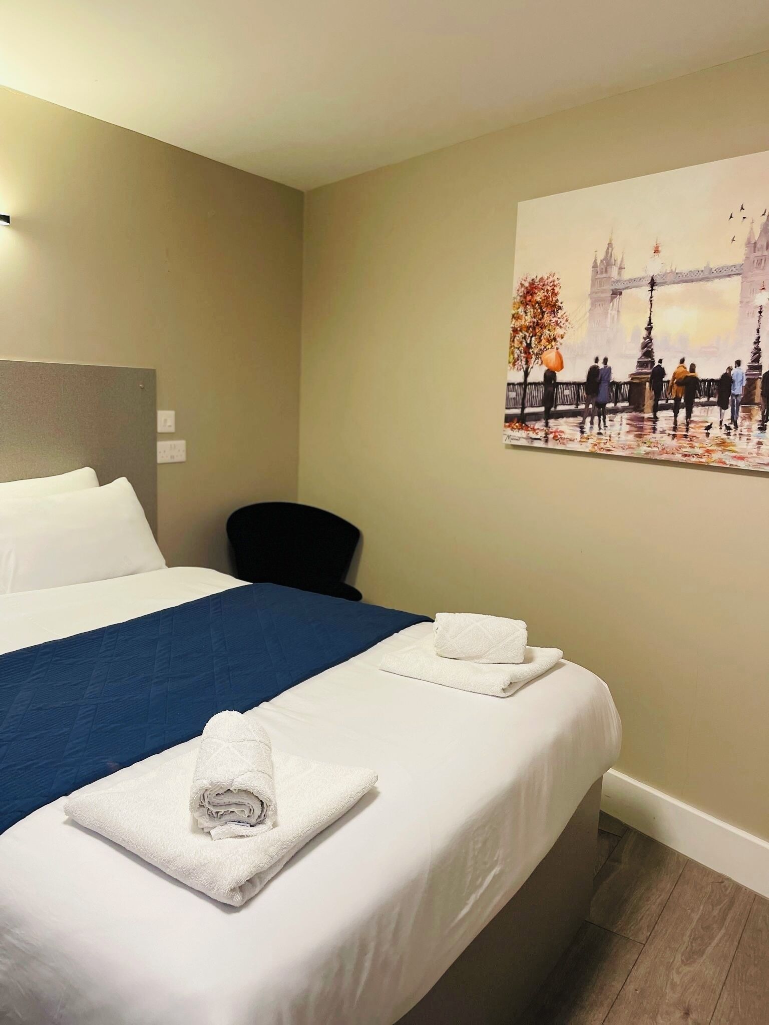 Una habitación de hotel con una cama, una silla y un cuadro de un puente.