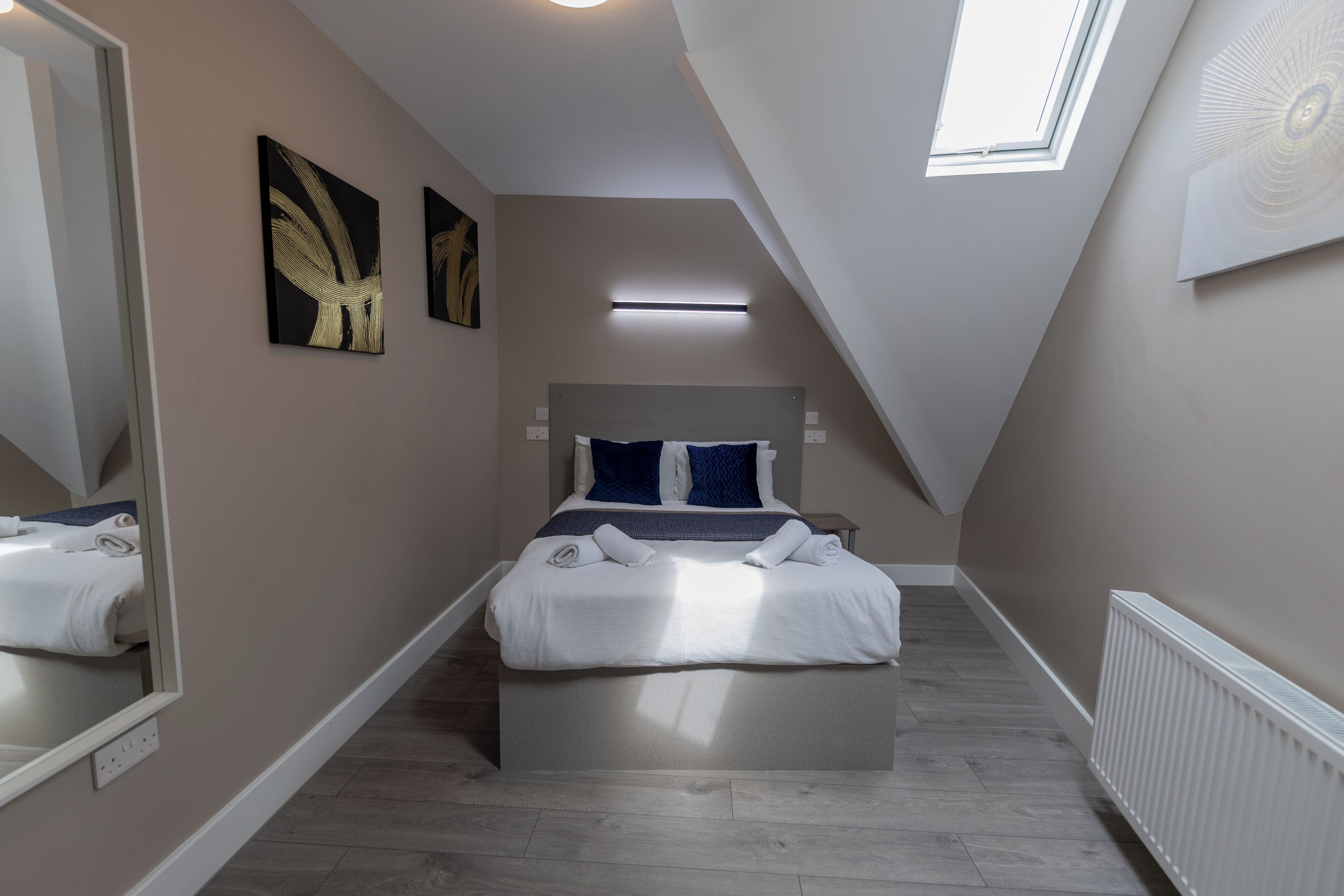 A modern bedroom with a skylight, a bed with white linens, and artwork on the walls.