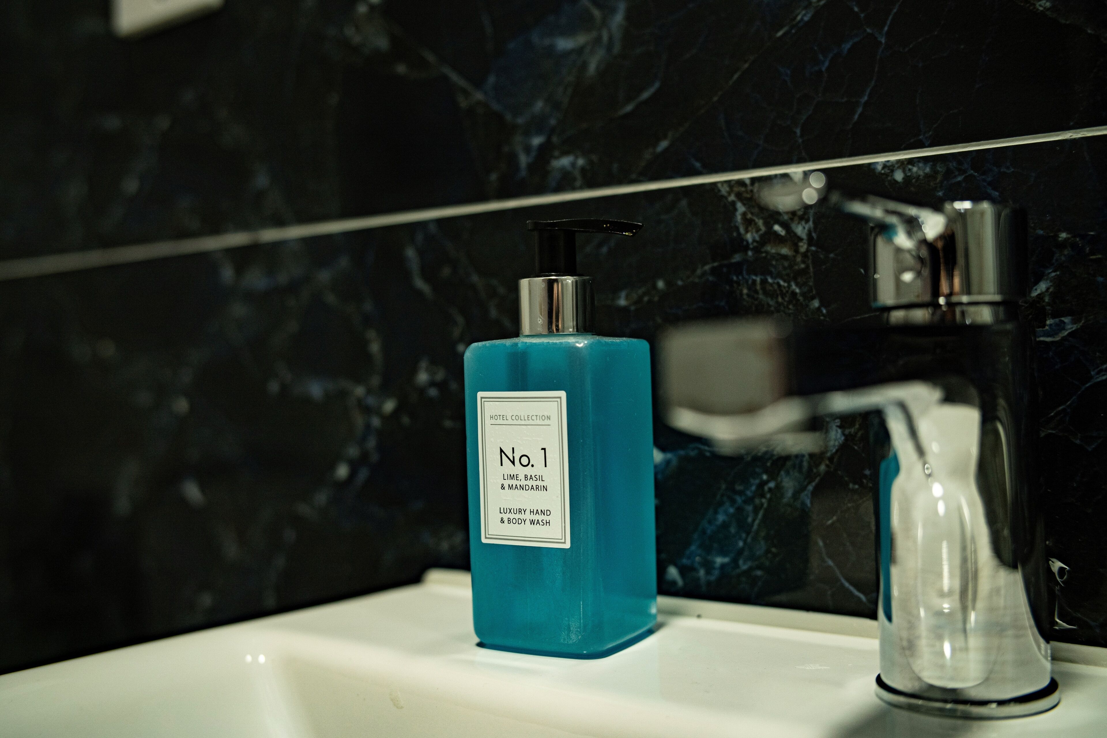 A bathroom with a marble sink, a blue hand soap dispenser, and a modern faucet.
