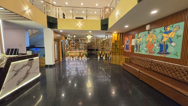 Un hall d’hôtel moderne avec un comptoir d’accueil en marbre, un coin salon doté d’un canapé marron et une grande fresque représentant des personnages traditionnels.