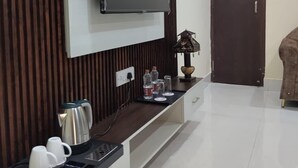 Un salon moderne avec un téléviseur à écran plat fixé à un mur en bois, un coin café avec une bouilloire et des tasses, et une porte visible au fond.