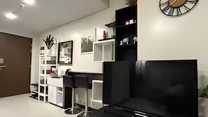 A modern living room with a black entertainment unit, white shelving, and a wall clock. - Charming, Comfy and Stylish Condo Stay! (Makati City)