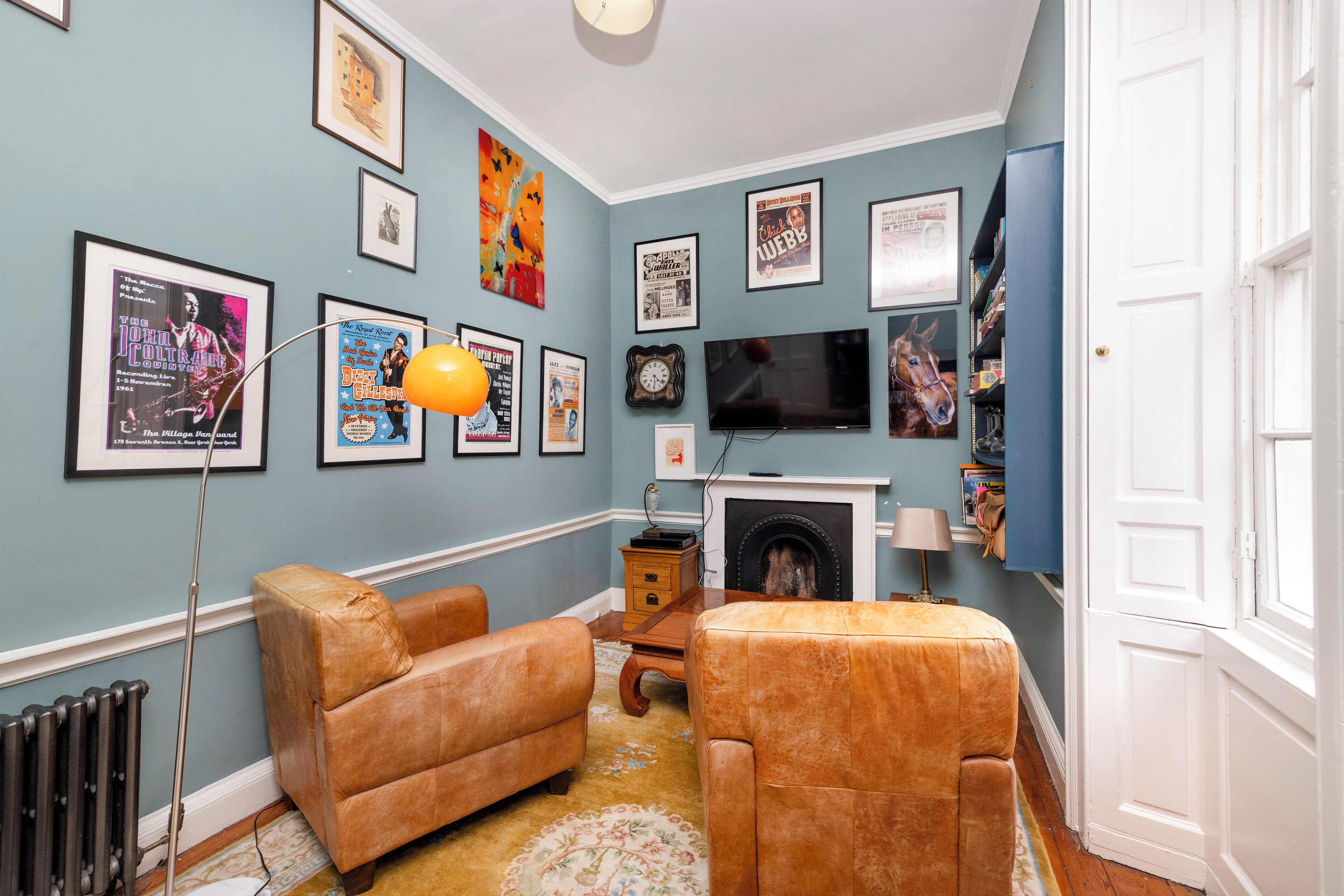 A living room with a fireplace, framed posters on the wall, a television, and a bookshelf.
