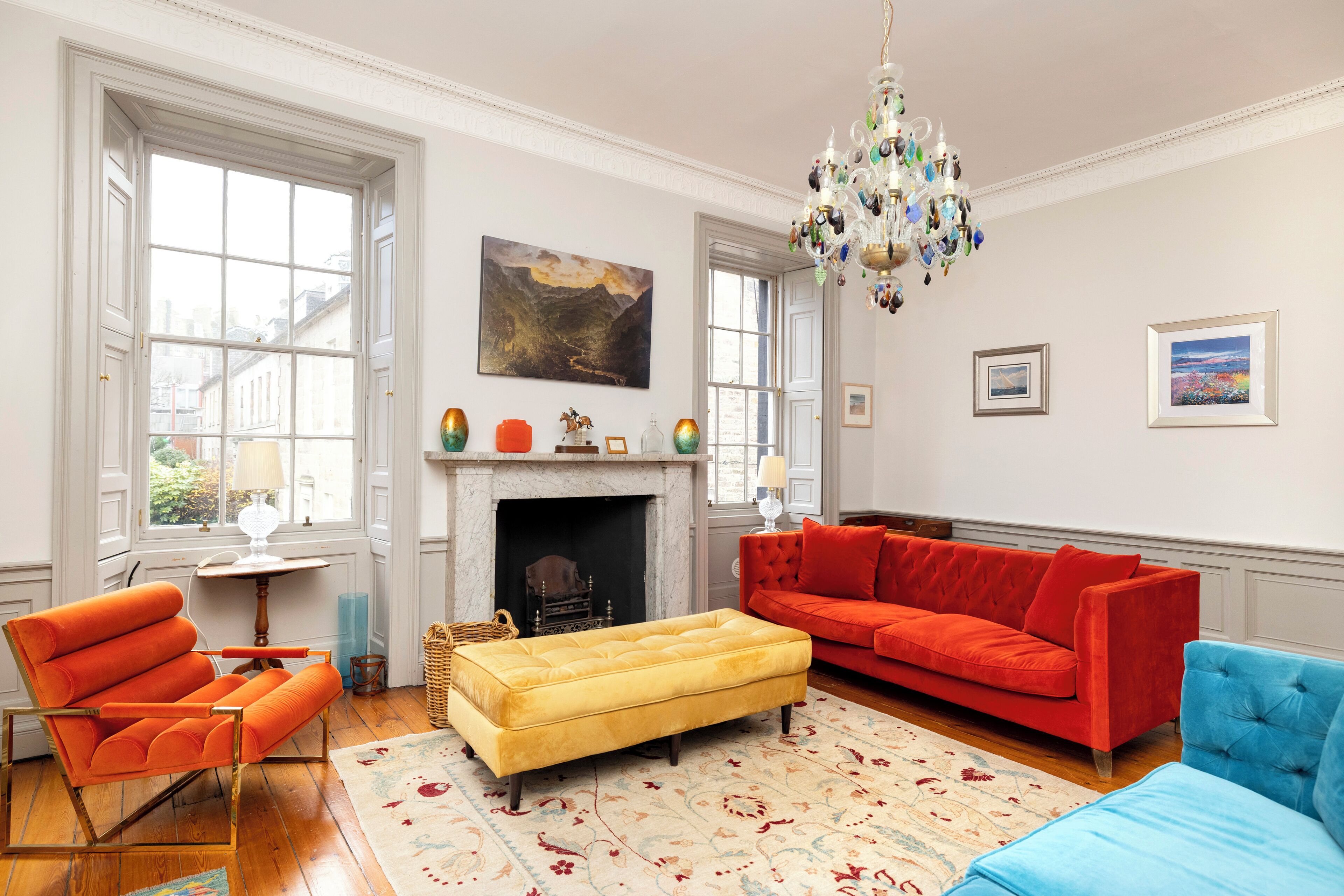 Una sala de estar con chimenea, un sofá rojo, un reposapiés amarillo y un sillón azul.